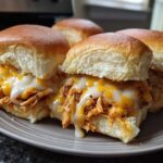 Close-up of several gooey Baked Buffalo Chicken Sliders featuring shredded chicken and melted white and orange cheese on soft rolls.