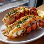 Two perfectly cooked Broiled Lobster Tail halves served on a white plate with melted butter and fresh parsley.