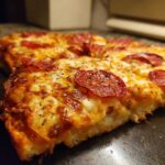 Extreme close-up of a thick slice of pepperoni pizza showing melted cheese and herbs, illustrating the texture of the Heart Shaped Pizza.