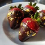Four decadent Chocolate Dipped Strawberries with Edible Gold Leaf resting on a white plate.