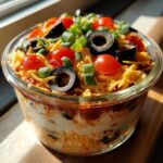 Close-up of Individual 7-Layer Dip Cups topped with shredded cheese, black olives, tomatoes, and green onions.
