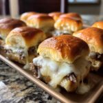 Close-up of gooey, melted cheese dripping over savory beef inside fresh Philly Cheesesteak Sliders on a baking tray.