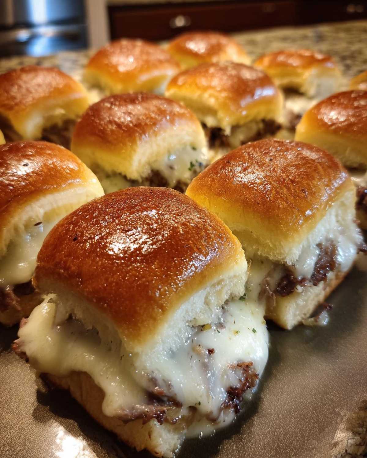 Close-up of freshly baked Philly Cheesesteak Sliders with melted white cheese oozing out.