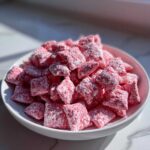 A white bowl filled with bright pink, powdered sugar-dusted Valentine’s Strawberry Muddy Buddies.