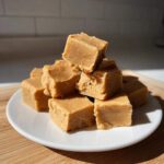 A tempting stack of homemade peanut butter fudge cubes piled high on a white plate.