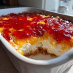 A scoop taken out of a baked pepper jelly cheese dip showing layers of crust, cream cheese, and bright red pepper jelly topping.