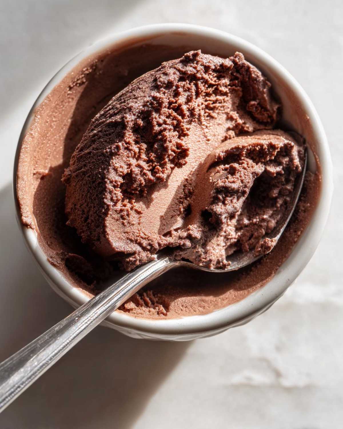 Overhead view of a spoonful of rich, dark chocolate mousse being lifted from a white bowl.