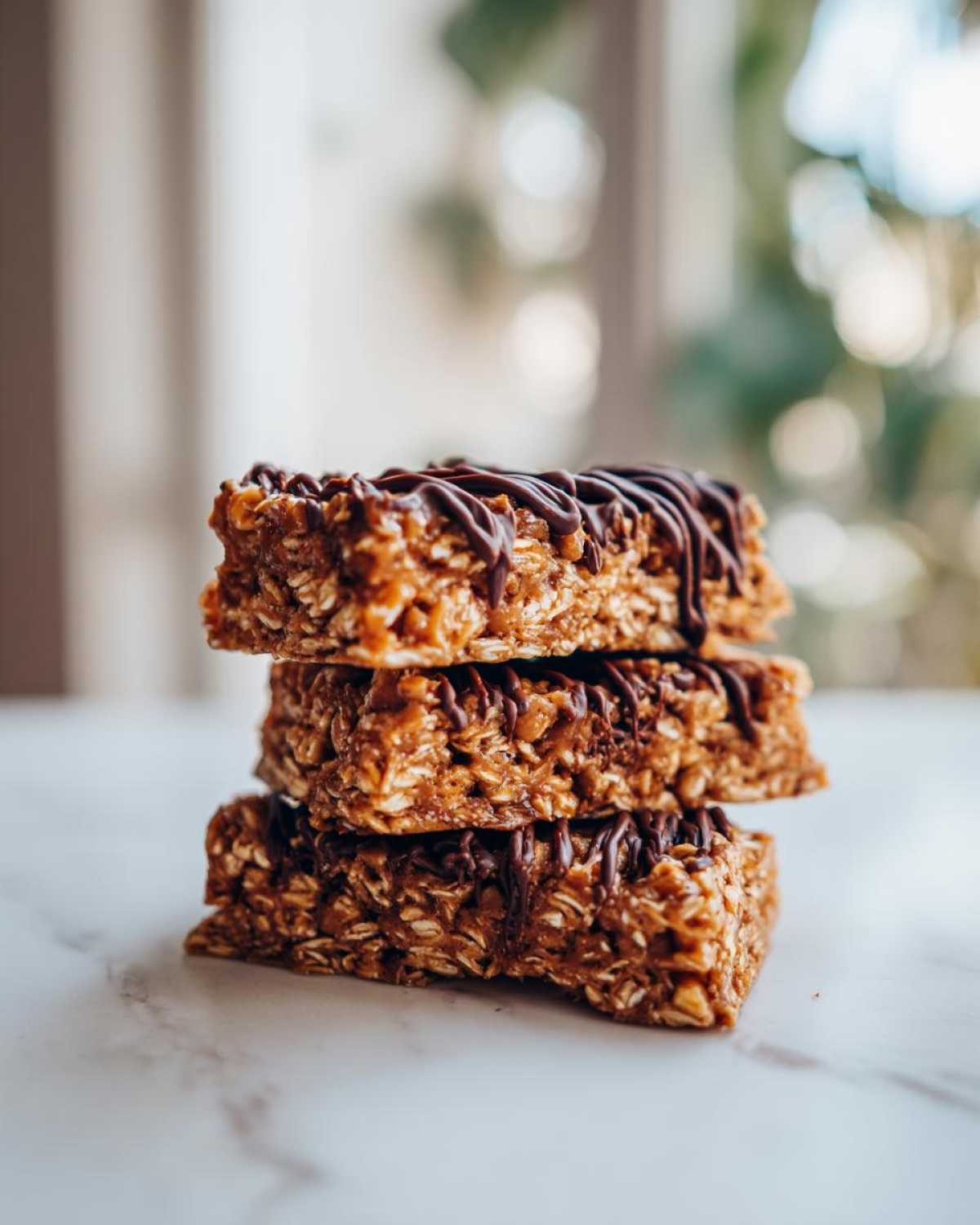 A stack of three homemade protein bars made with oats and drizzled with dark chocolate.