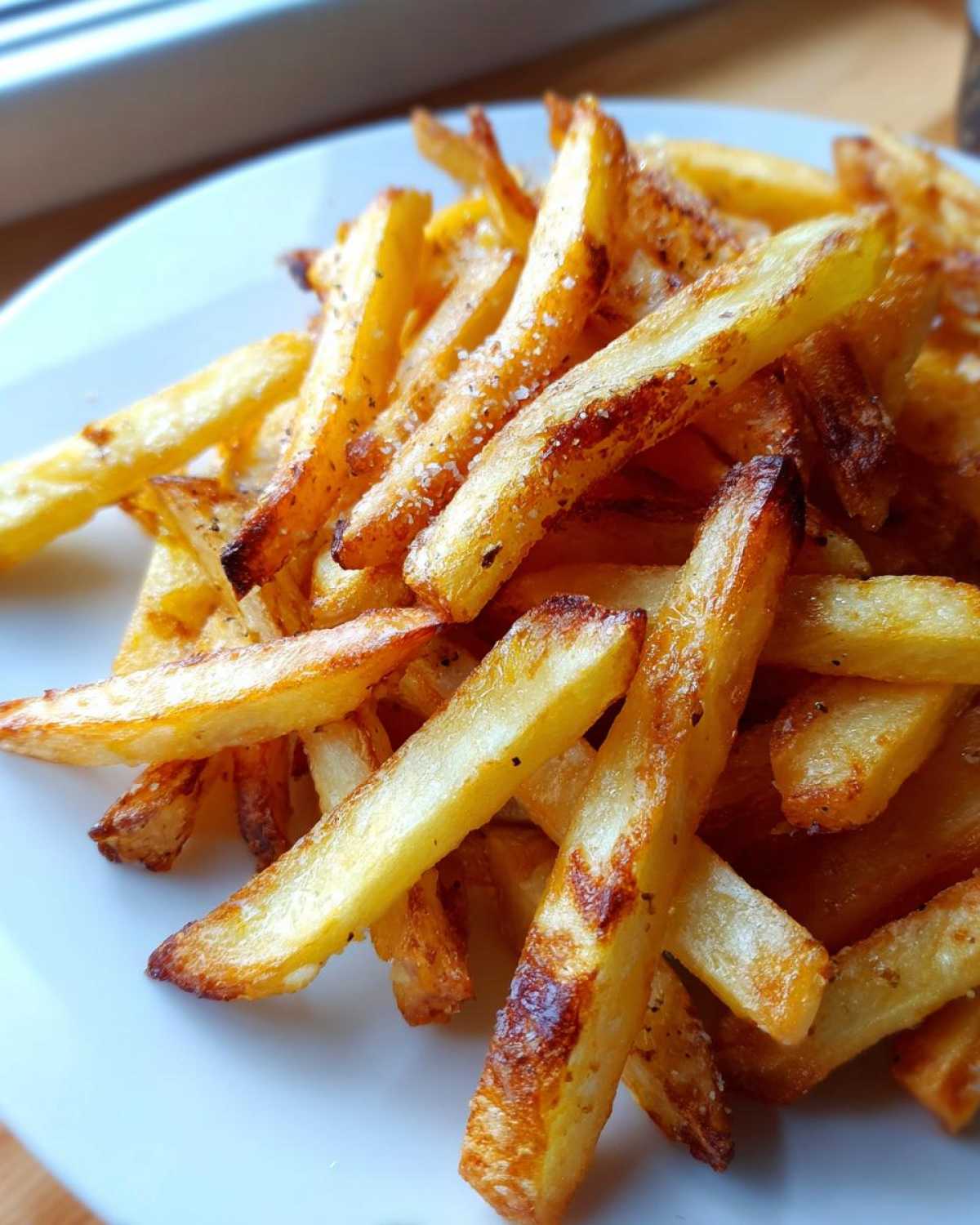 Close-up of golden, crispy air fryer french fries seasoned with salt, piled on a white plate.