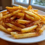 A close-up of a white plate piled high with golden, crispy air fryer french fries sprinkled with salt.