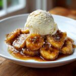 Close-up of caramelized bananas in rich sauce topped with vanilla ice cream, a perfect bananas foster dessert.