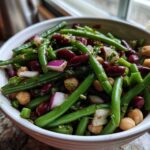 Close-up of a white bowl filled with vibrant green bean salad featuring green beans, kidney beans, chickpeas, and red onion.
