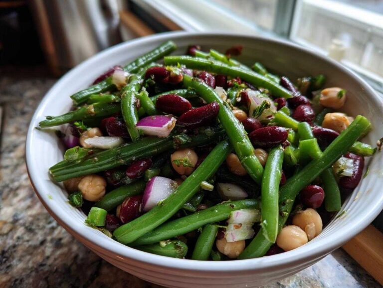 Amazing 220 Calorie bean salad recipe Close-up of a white bowl filled with vibrant green bean salad featuring green beans, kidney beans, chickpeas, and red onion.
