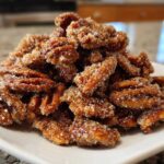 A close-up of a mound of freshly made cinnamon sugar pecans piled high on a white plate.