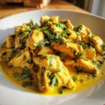 Close-up of tender pieces of coconut chicken coated in a rich, yellow coconut sauce and topped with fresh cilantro.