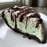 A close-up slice of no bake grasshopper pie with mint filling, whipped topping, and chocolate drizzle.