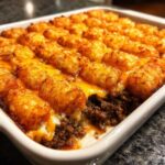 Close-up of a freshly baked tater tot casserole showing crispy tots, melted cheddar cheese, and seasoned ground beef layer.