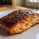 Close-up of a perfectly cooked piece of blackened salmon with a dark, spicy crust resting on a white plate.