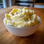 A fluffy bowl of creamy Boursin mashed potatoes topped with black pepper and herbs.
