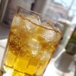 Close-up of a tall glass filled with bubbly, golden lemonade and ice cubes, suggesting a refreshing drink.