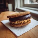 A close-up of a no-bake buckeye graham crackers sandwich cookie with peanut butter filling and chocolate topping.
