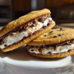 Two delicious cannoli cookies sandwiched with creamy filling and mini chocolate chips, resting on a white plate.