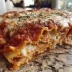 A close-up, cross-section view of a cheesy baked ravioli casserole slice oozing sauce and melted cheese.