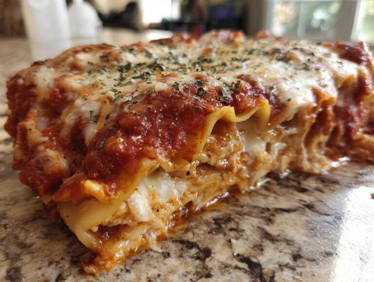 A close-up, cross-section view of a cheesy baked ravioli casserole slice oozing sauce and melted cheese.