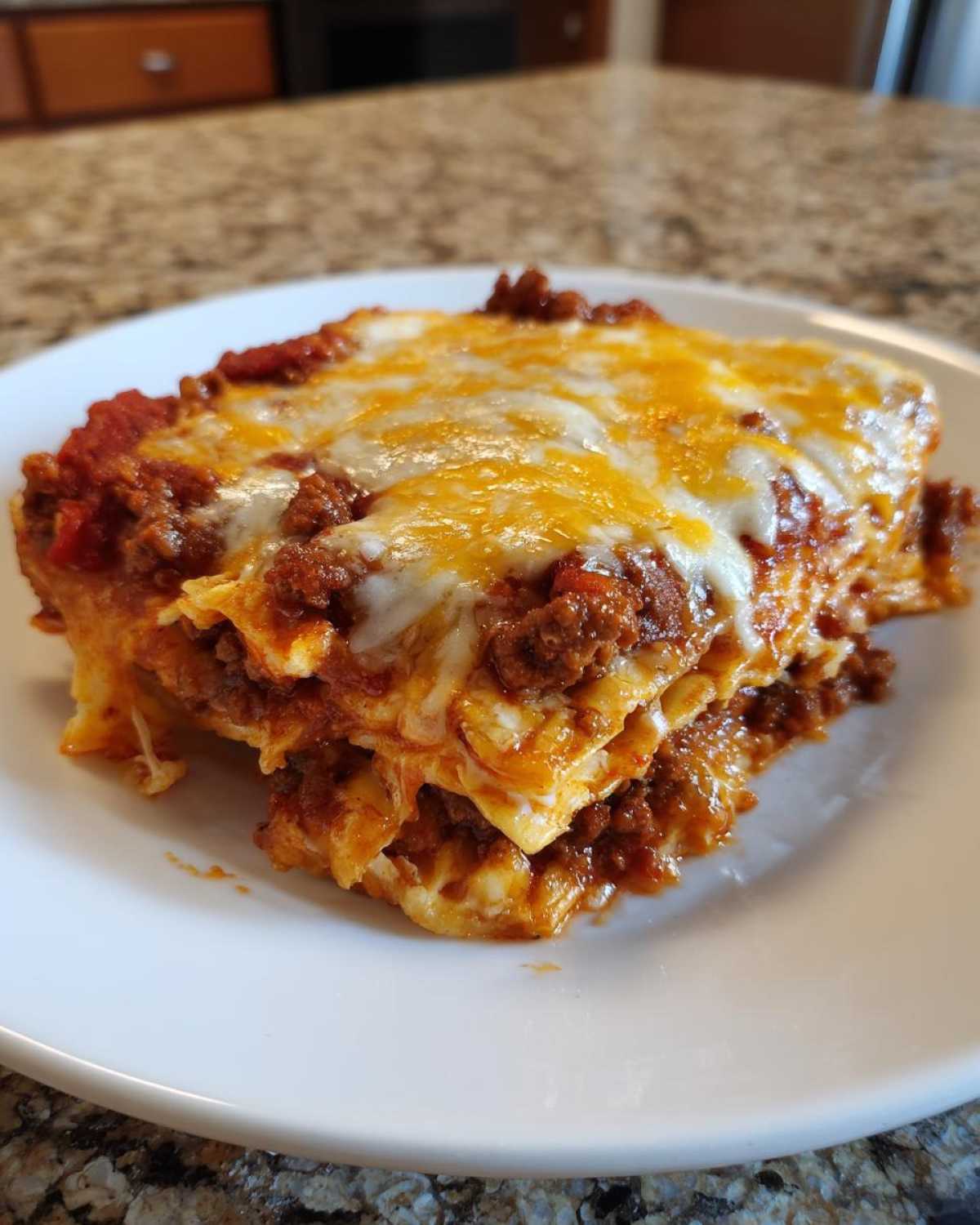 A close-up of a cheesy, layered slice resembling Mexican pizza on a white plate.