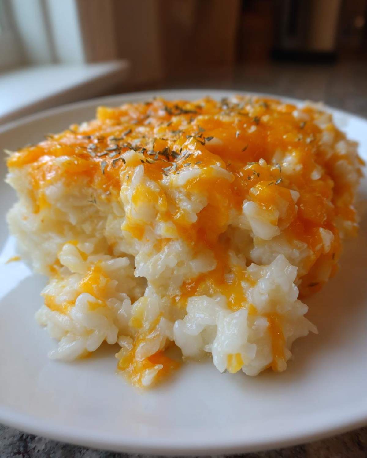 A close-up serving of creamy, white cheesy rice topped with melted orange cheddar cheese and dried herbs.