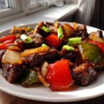 A close-up of glistening, saucy Chinese pepper steak mixed with vibrant red and green bell peppers and onions.