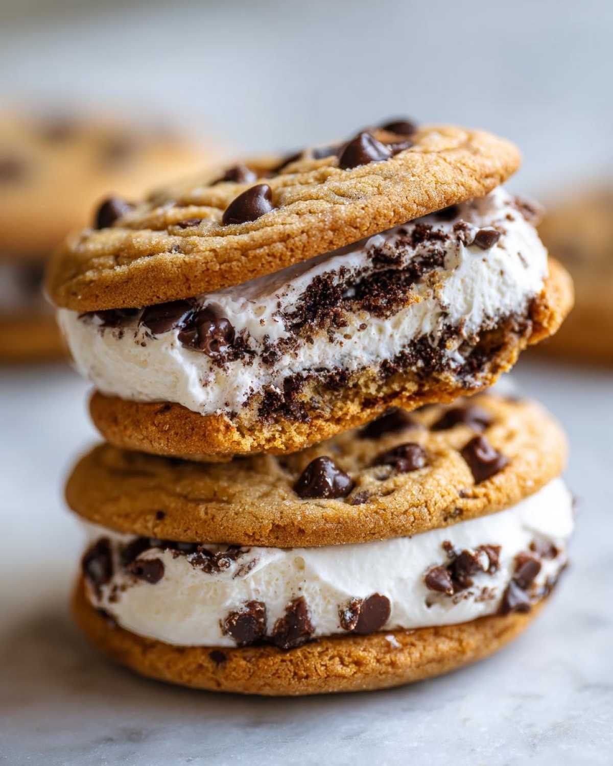 Two stacked chocolate chip cookie sandwiches filled with creamy white filling, resembling cannoli cookies.