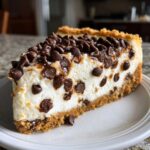 A generous slice of rich chocolate chip cheesecake featuring a thick graham cracker crust and topped with melted chocolate chips.