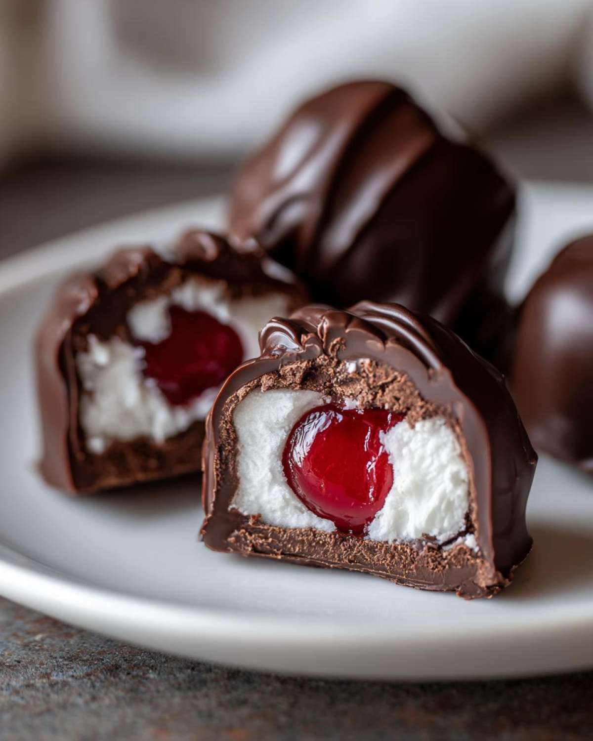 Close-up of a chocolate covered cherries treat cut in half, showing a white creamy center and a bright red cherry inside.