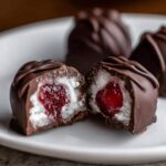 Close-up of a chocolate covered cherries treat cut in half, showing the white coconut filling and bright red cherry center.