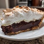 A close-up view of a thick slice of chocolate meringue pie showing the dark chocolate filling and toasted meringue topping.