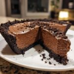 A close-up of a rich chocolate mousse pie with a thick, dark crust, sliced open to show the creamy filling.