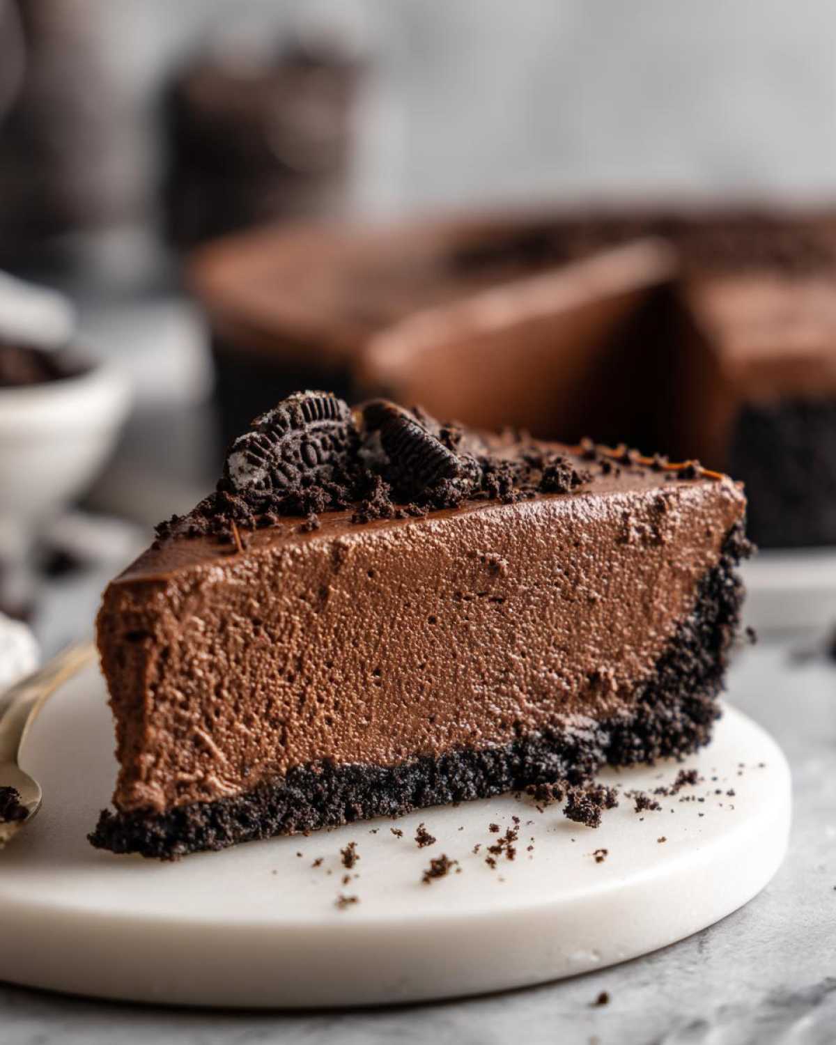 A thick slice of decadent chocolate mousse pie with a dark cookie crust, topped with crushed cookies and an Oreo half.