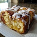 Close-up of a serving of cinnamon roll french toast, drizzled heavily with white icing.