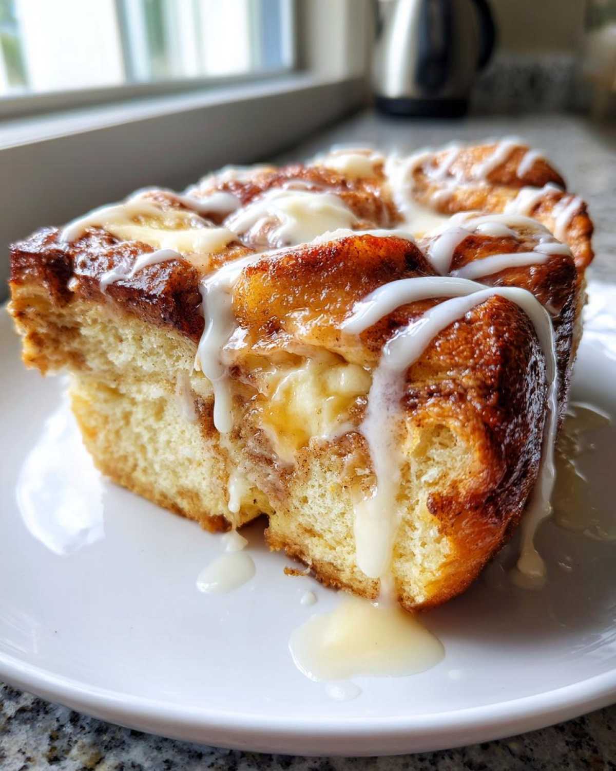 A close-up of a decadent slice of cinnamon roll french toast drizzled heavily with white icing.