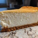A thick, creamy slice of classic cheesecake with a golden top and graham cracker crust, showcasing the amazing cheesecake recipe texture.