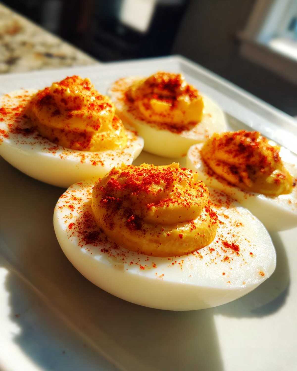 Four halves of classic deviled eggs topped with creamy yolk filling and sprinkled with bright red paprika.