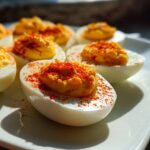 Close-up of several classic deviled eggs garnished with paprika on a white platter.
