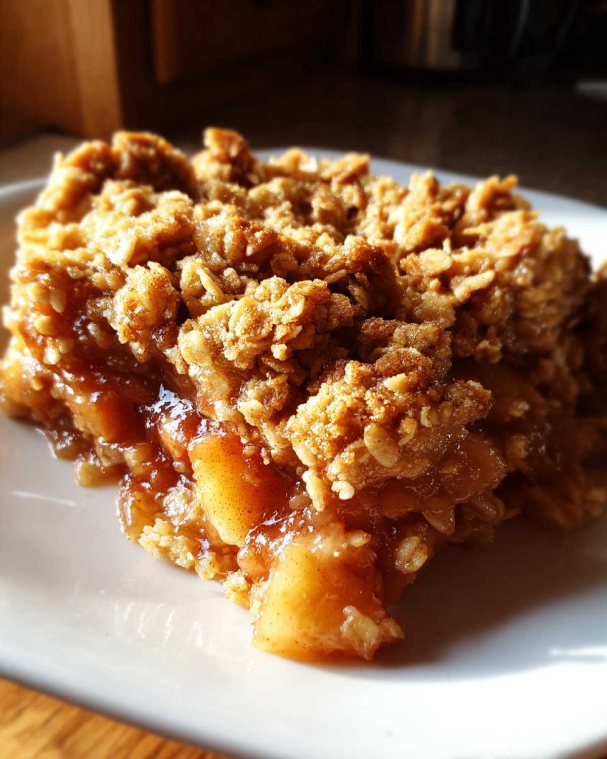 A close-up, mouthwatering slice of apple crisp recipe showing warm, gooey cinnamon apples beneath a thick, crunchy oat topping.