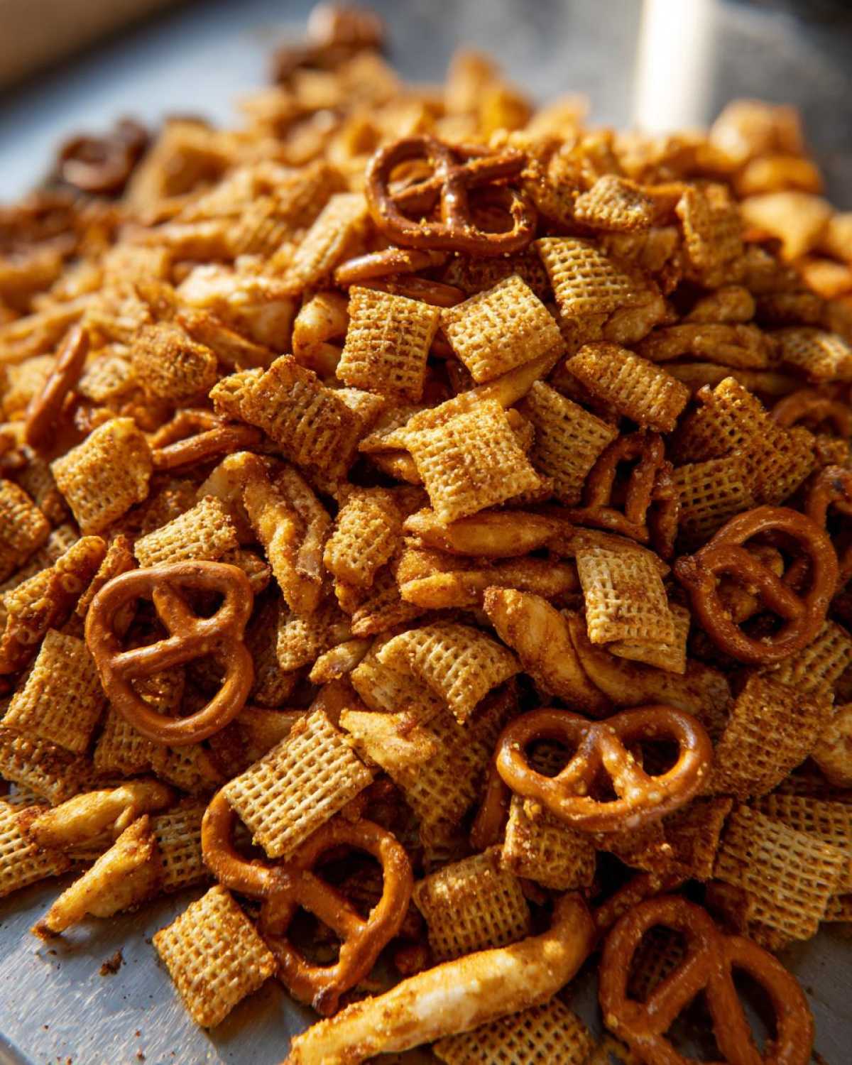 A close-up, high-angle shot of a large pile of seasoned chex party mix featuring Chex cereal and mini pretzels.