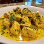 Close-up of tender pieces of coconut chicken served in a rich, yellow, creamy sauce and garnished with fresh cilantro.
