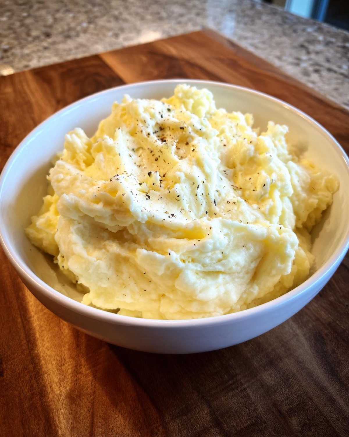 A white bowl filled with creamy Boursin mashed potatoes, topped with cracked black pepper.