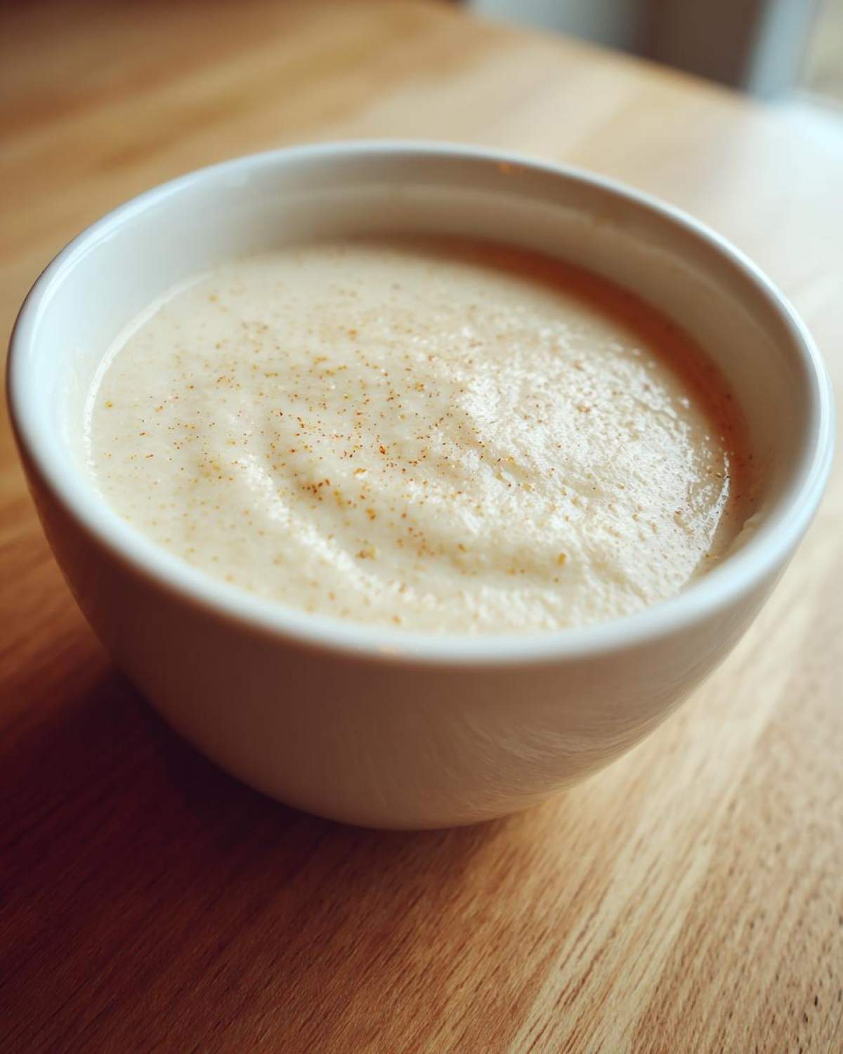 Close-up of a creamy cauliflower soup served in a white bowl, lightly dusted with spices.