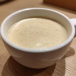 Close-up of a small white mug filled with smooth, creamy cauliflower soup, lightly dusted with spice.