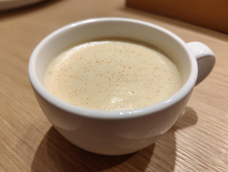 Close-up of a small white mug filled with smooth, creamy cauliflower soup, lightly dusted with spice.